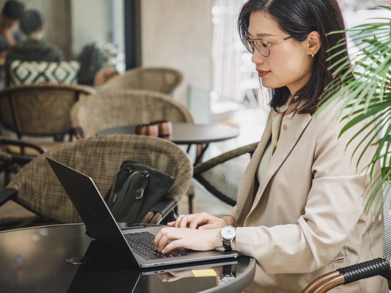 Eine asiatische Frau sitzt in einem Café und bearbeitet ihre Bewerbung am Laptop.l