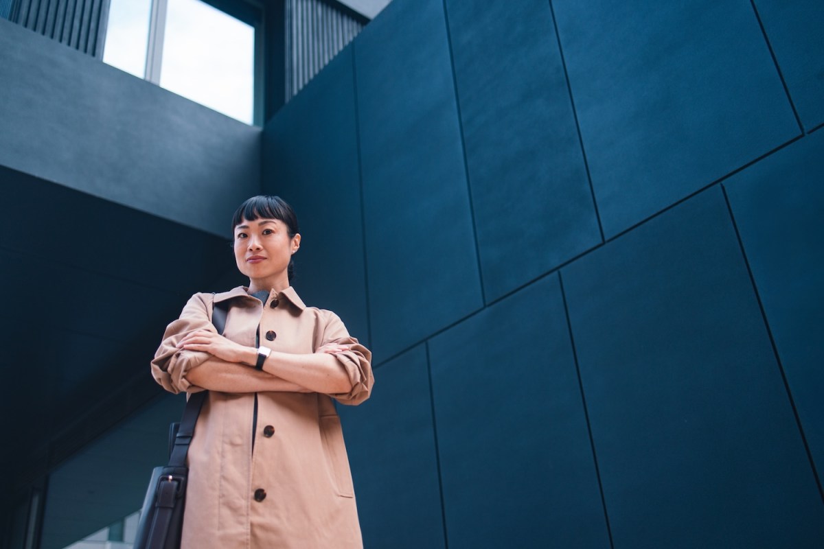 Frau posiert selbstbewusst im Freien vor einem Gebäude.