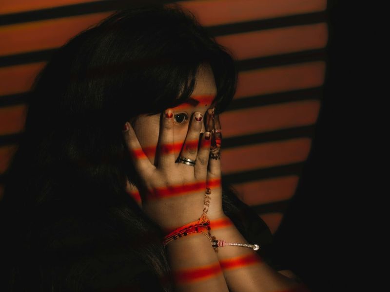 Eine Frau mit roten Lichtstreifen im Gesicht hält sich die Hände vors Gesicht.