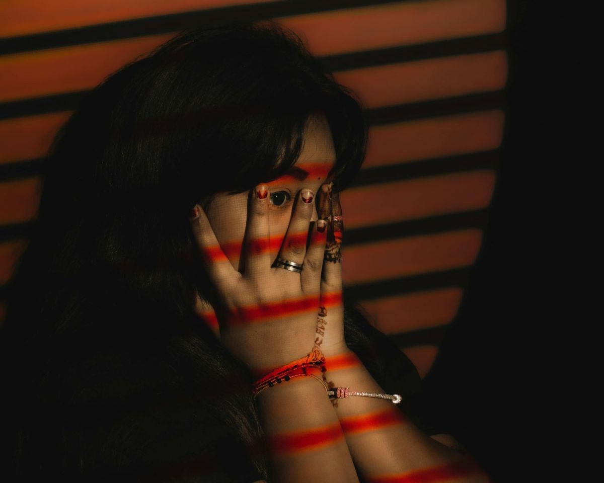 Eine Frau mit roten Lichtstreifen im Gesicht hält sich die Hände vors Gesicht.