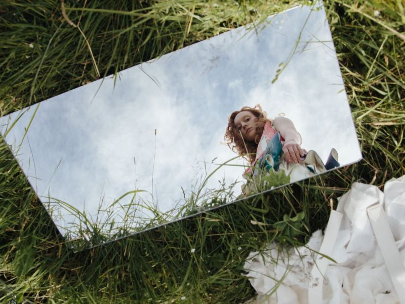 Ein Spiegel liegt im Gras und im Spiegelbild sieht man eine Frau, die hineinschaut.