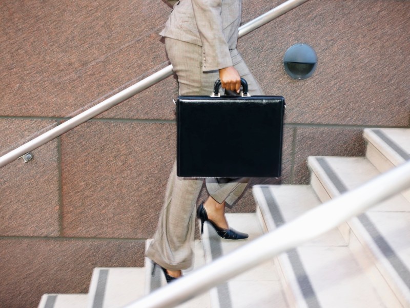 Eine Frau mit einer schwarzen Aktentasche läuft eine Treppe hoch.