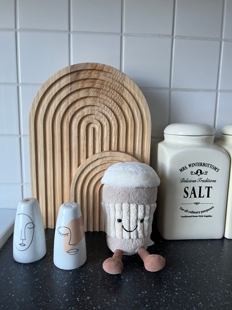 Kaffeebecher-Jellycat sitzt in der Küche vor einem Schneidebrett.