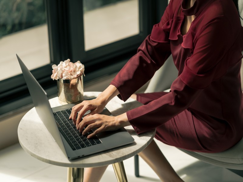 Eine Frau im roten Kleid tippt auf dem Laptop.