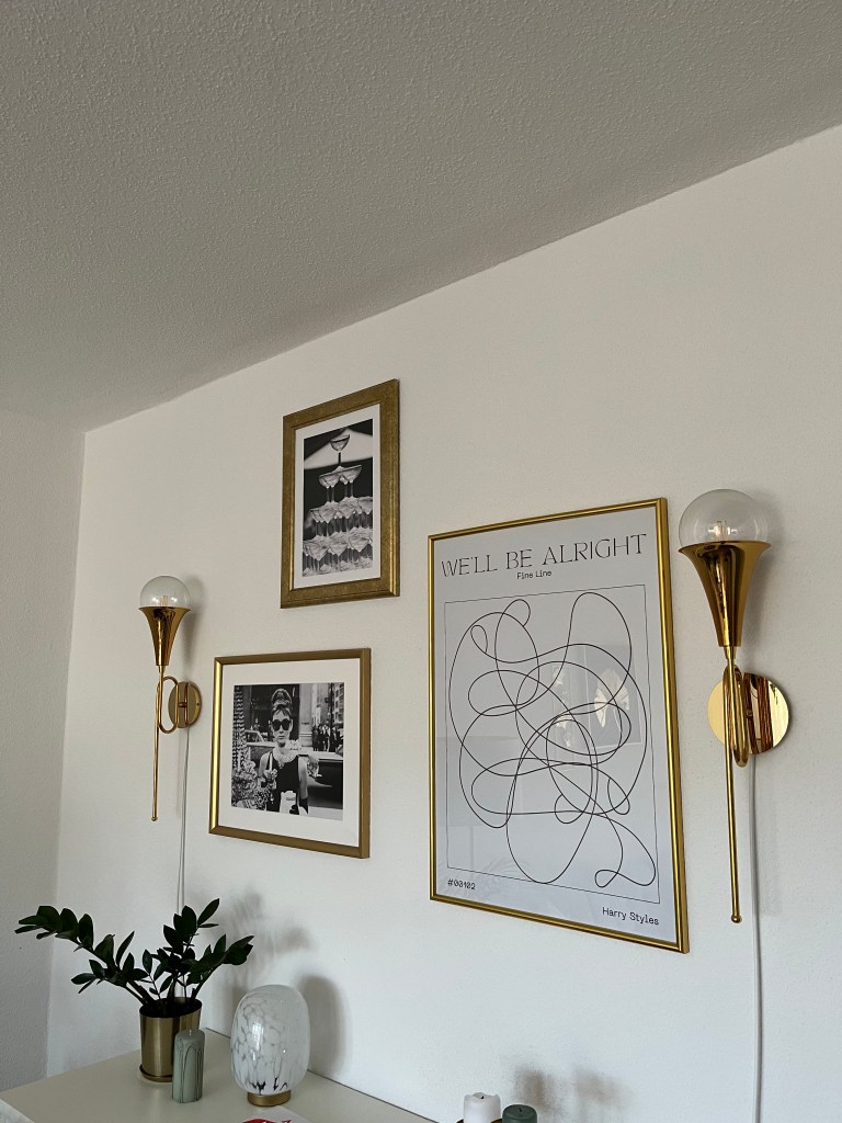 3 Poster an einer Wand in einem Wohnzimmer zwischen zwei Lampen.