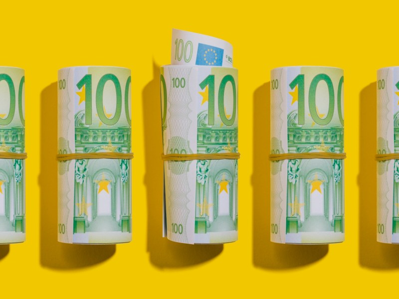 100-Euro-Rollen liegen flach auf gelbem Hintergrund.