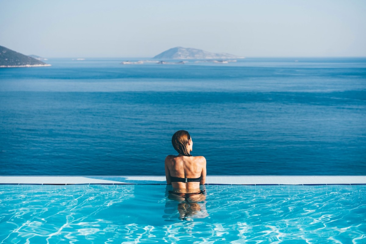 Frau im Infinity-Pool bewundert malerische Aussicht.