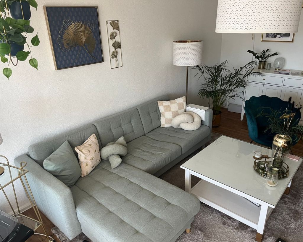 Ein Wohnzimmer mit einer mintgrünen Couch und Kissen in verschiedenen Formen darauf.