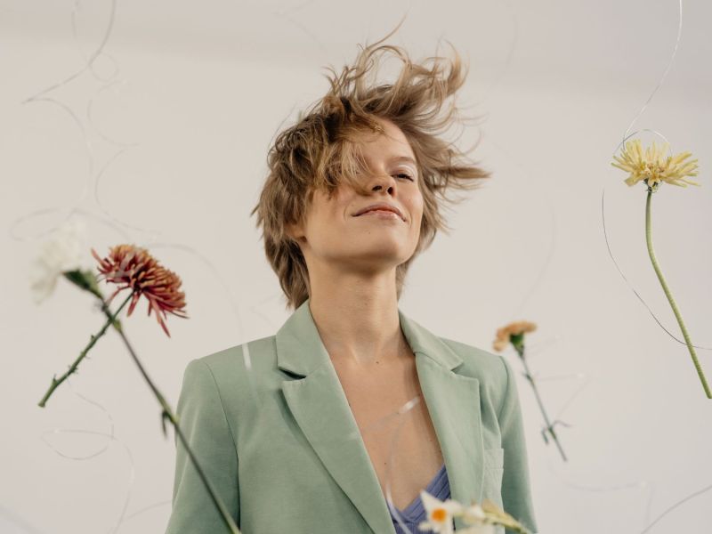 Frau mit Wind in den Haaren und Blumen, die an Fäden um sie herum schweben.