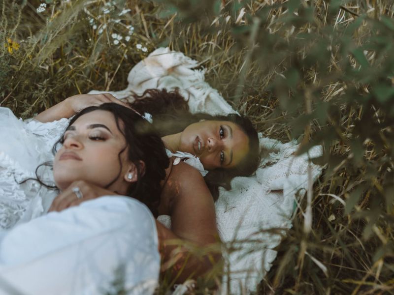 Zwei Frauen liegen auf einer weißen Decke auf einer Wiese.