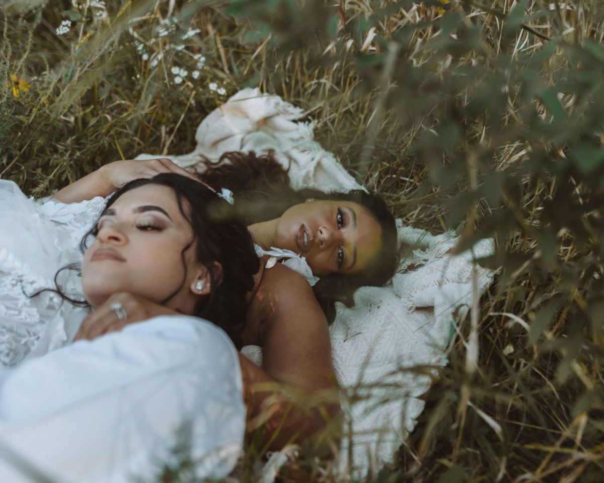 Zwei Frauen liegen auf einer weißen Decke auf einer Wiese.