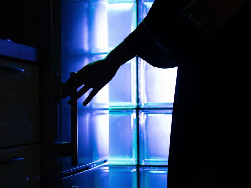 Arm öffnet einen Kühlschrank vor dem Hintergrund eines blau belichteten Fensters