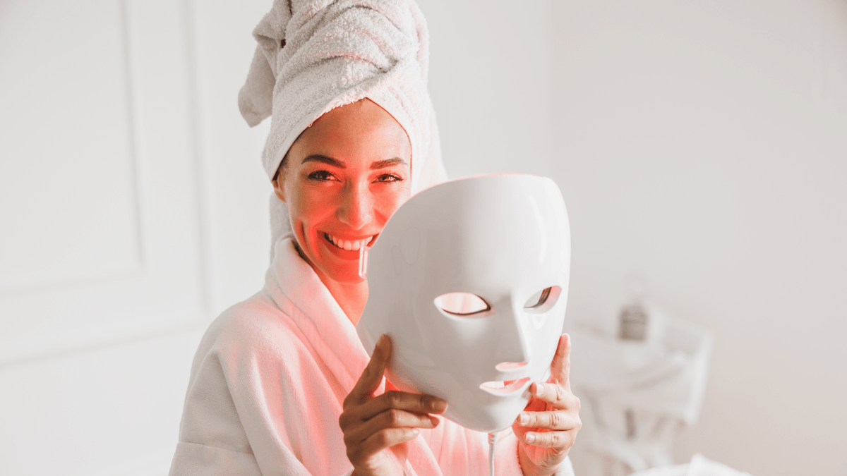 Frau lacht, hat ein Handtuch auf dem Kopf und hält eine LED Maske