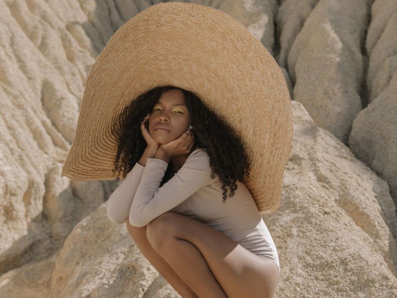 Frau mit übergroßem Hut in einer trockenen Landschaft