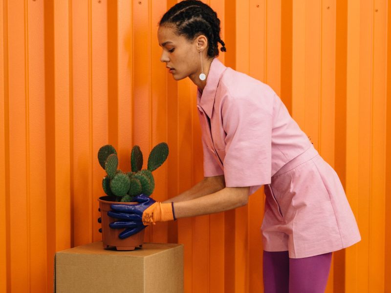 Frau kümmert sich vor einer orangefarbenen Wand um einen Kaktus.