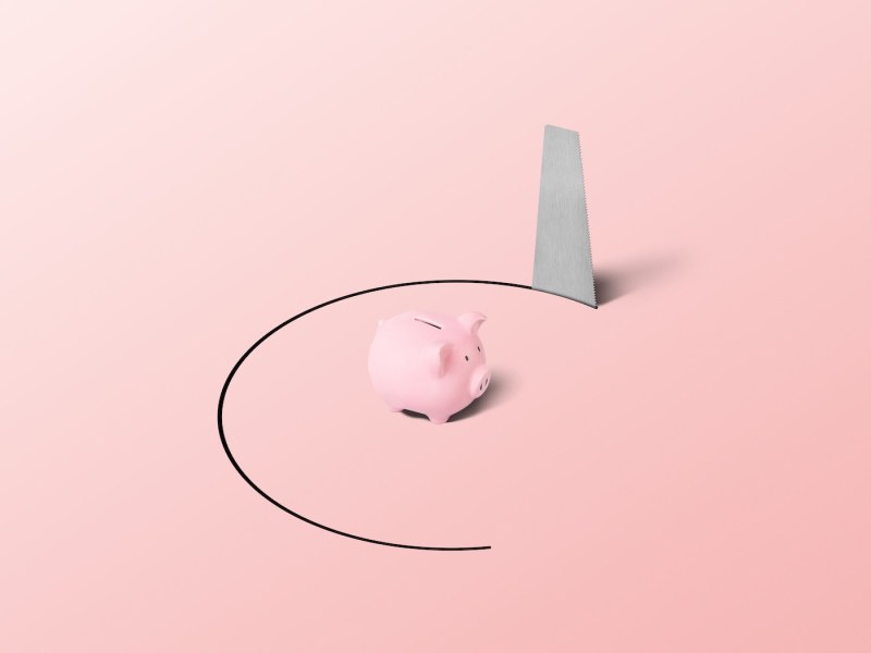 Ein Sparschwein in einer gefangenen Position mit einer Handsäge.