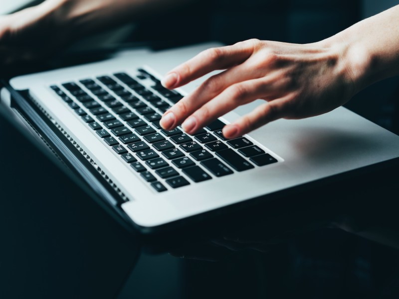 Eine Nahaufnahme einer Frauenhand, die auf einem Laptop die Tasten drückt.