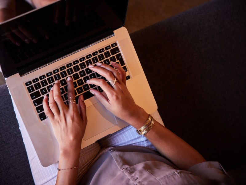Nahaufnahme einer Frau, die auf einem Sofa sitzt und mit einem Laptop online arbeitet