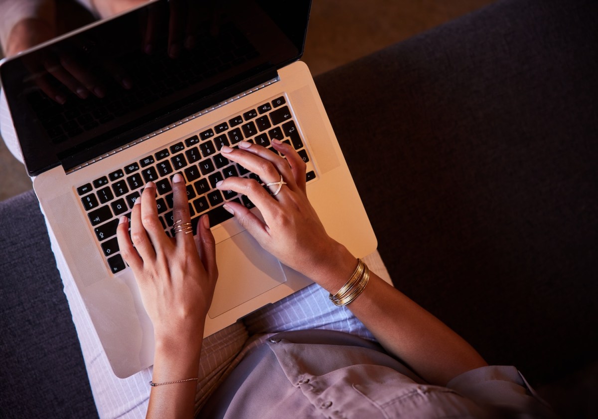 Nahaufnahme einer Frau, die auf einem Sofa sitzt und mit einem Laptop online arbeitet