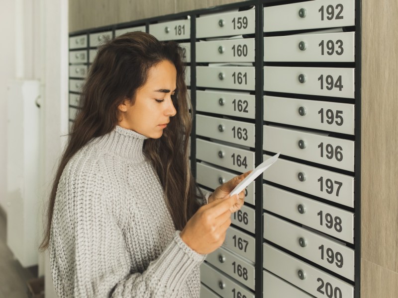 Frau schaut sich vor Briefkästen einen Brief an.