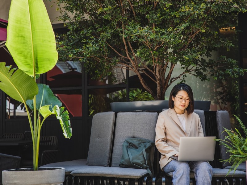 Asiatische Geschäftsfrau mit Laptop auf einem Outdoor-Stuhl sitzend.