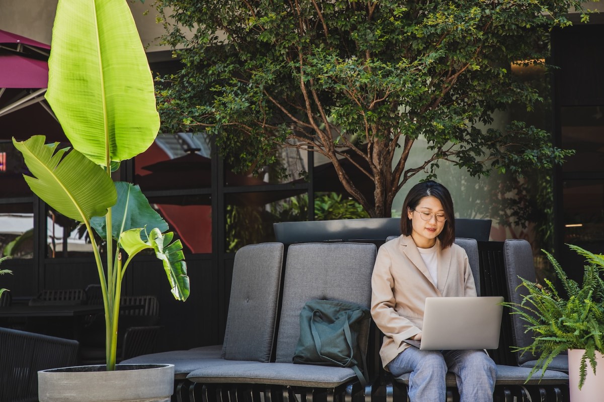 Asiatische Geschäftsfrau mit Laptop auf einem Outdoor-Stuhl sitzend.