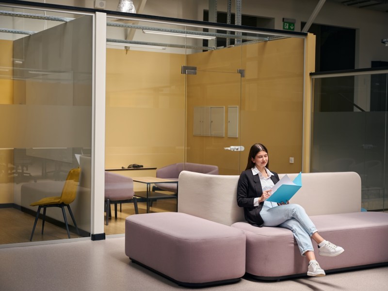 Frau in Jacke sitzt auf einem Sofa mit Dokumenten in einem blauen Ordner.