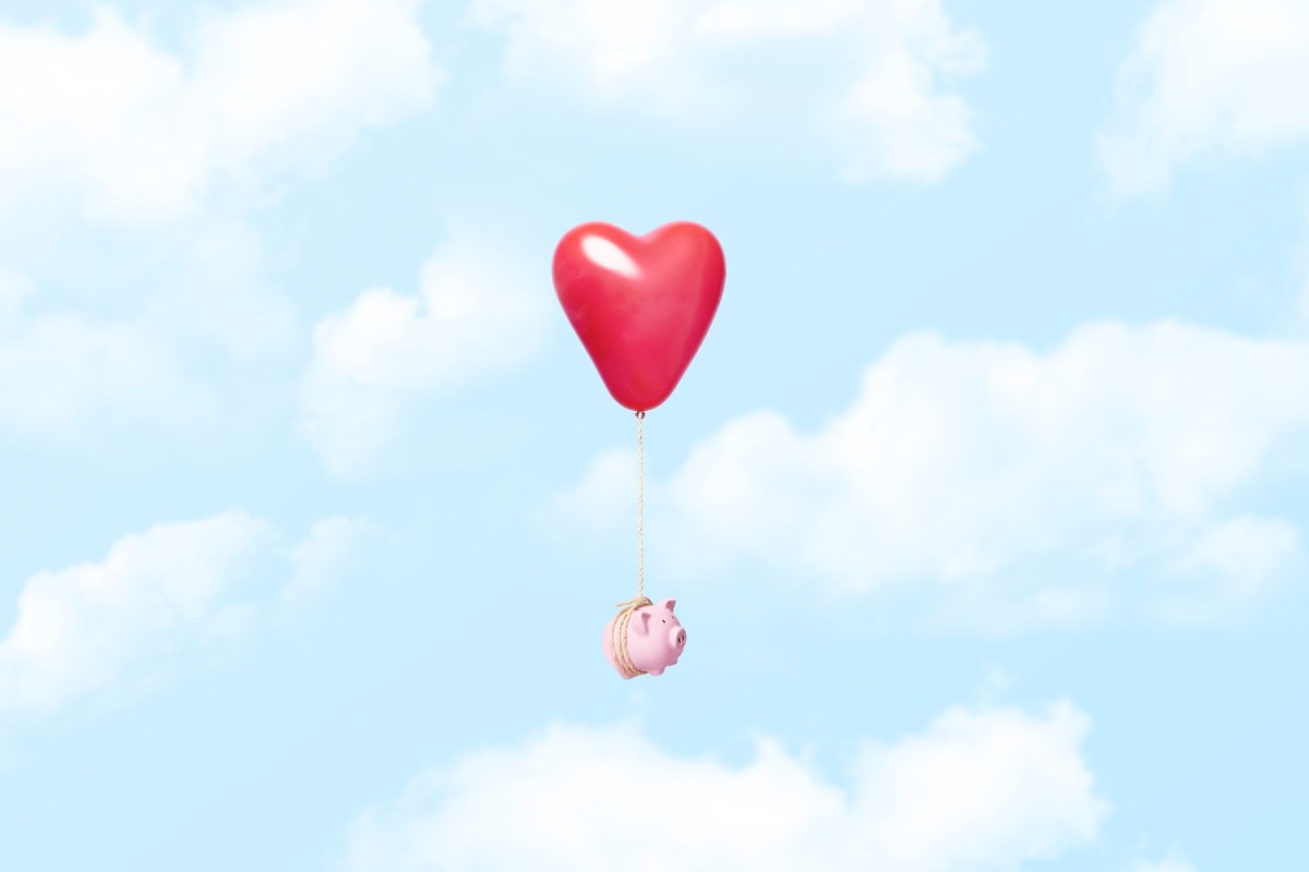 Horizontales Konzeptbild eines einzelnen rosa Sparschweins, das an einem roten Herzballon mit einem Seil befestigt ist, das durch die Wolken schwebt.