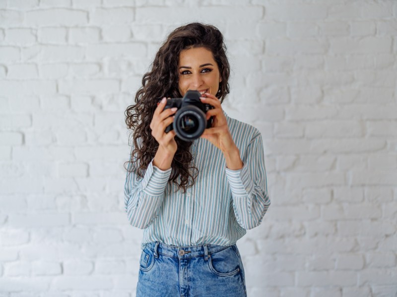 Frau hält eine Kamera in der Hand und lächelt.