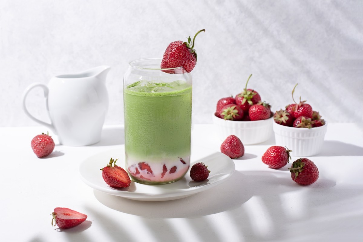 Glas mit Erdbeer-Matcha-Latte mit Erdbeeren auf weißem Hintergrund.
