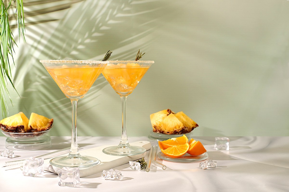 Cocktail mit Tequila, Rum und Wodka mit Ananasscheiben, Orange, Eis und Rosmarin.