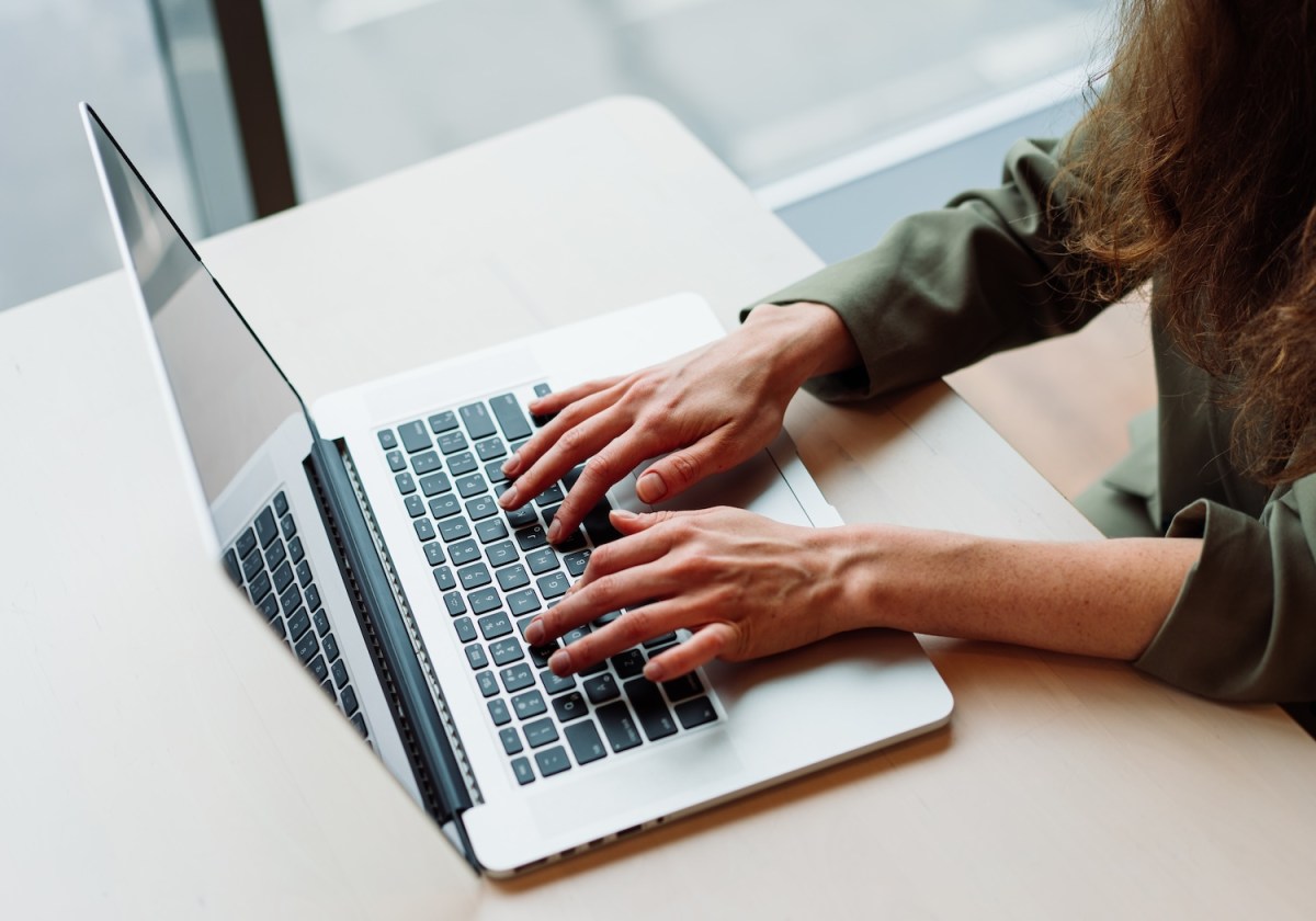 Eine Nahaufnahme einer berufstätigen Frau, die an einem modernen Büroschreibtisch mit einem Laptop arbeitet. Ihre Hände tippen auf der Tastatur.