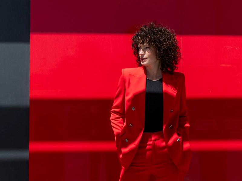 Selbstbewusste Geschäftsfrau mit Händen in den Taschen steht in der Nähe der roten Wand.