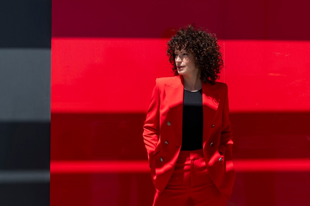 Selbstbewusste Gesch&auml;ftsfrau mit H&auml;nden in den Taschen steht in der N&auml;he der roten Wand.