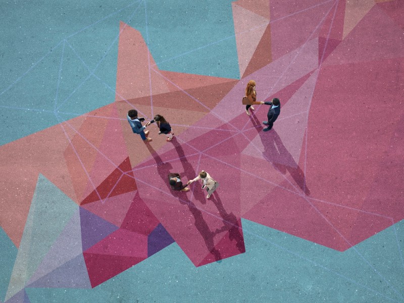 Geschäftsleute geben sich die Hand, während sie auf einem aufgemalten Muster auf Asphalt stehen.