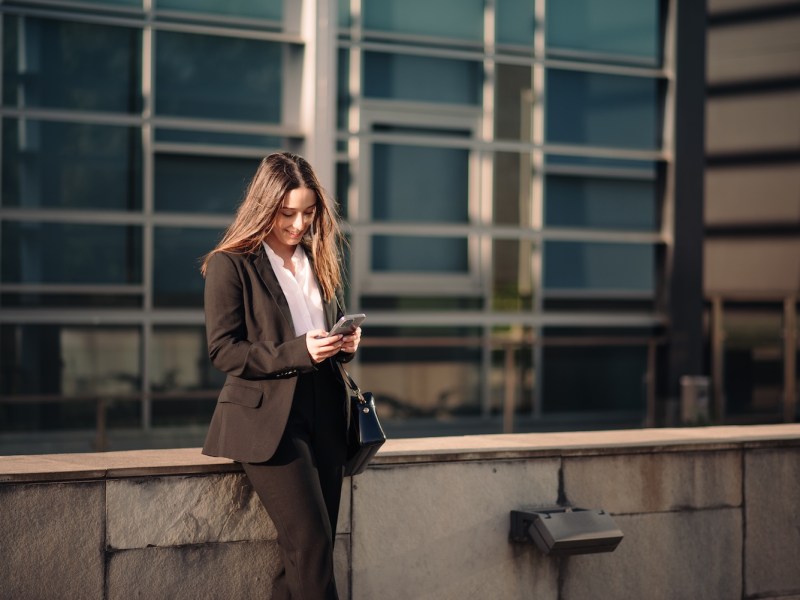 Junge Geschäftsfrau mit ihrem Smartphone in einem Bürogebäudebereich.