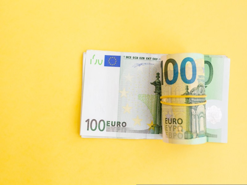 Geldrolle mit Euro-Banknoten mit einem Gummiband auf gelbem Hintergrund.