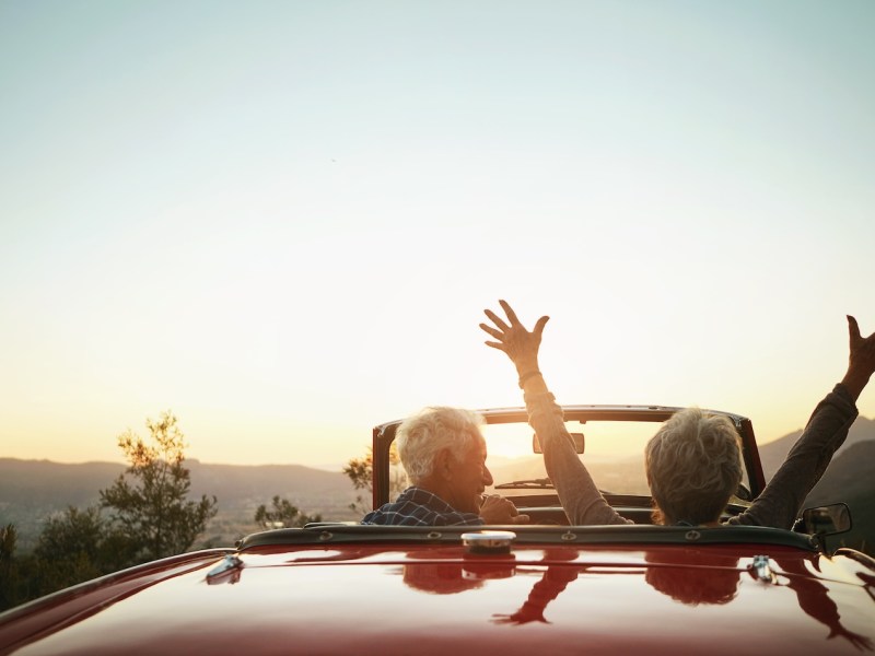 Ein Rentner-Paar sitzt bei Sonnenuntergang im Cabrio.