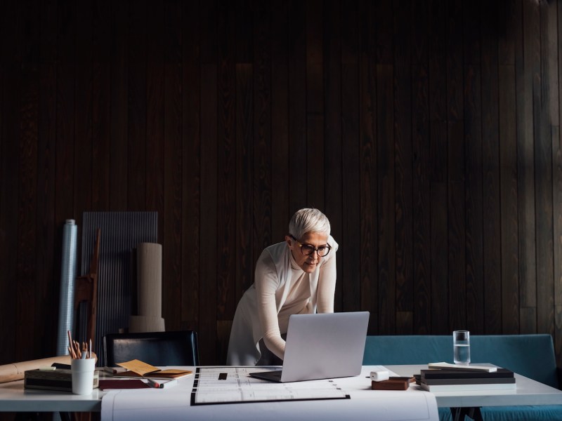 Multitasking: Eine elegante Architektin arbeitet von ihrem Homeoffice aus, nutzt ihren Laptop und entwirft ein neues Projekt.