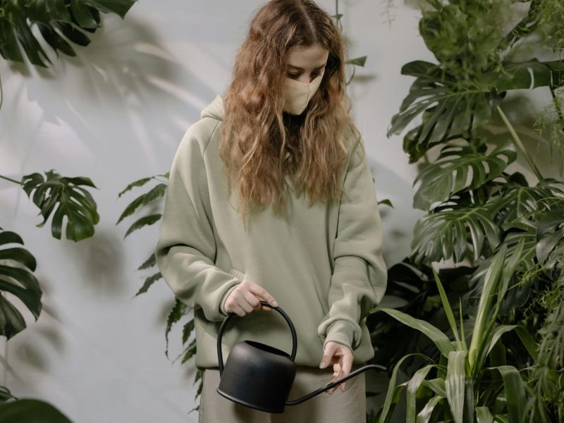 Frau mit einer Maske über dem Mund gießt Blumen.