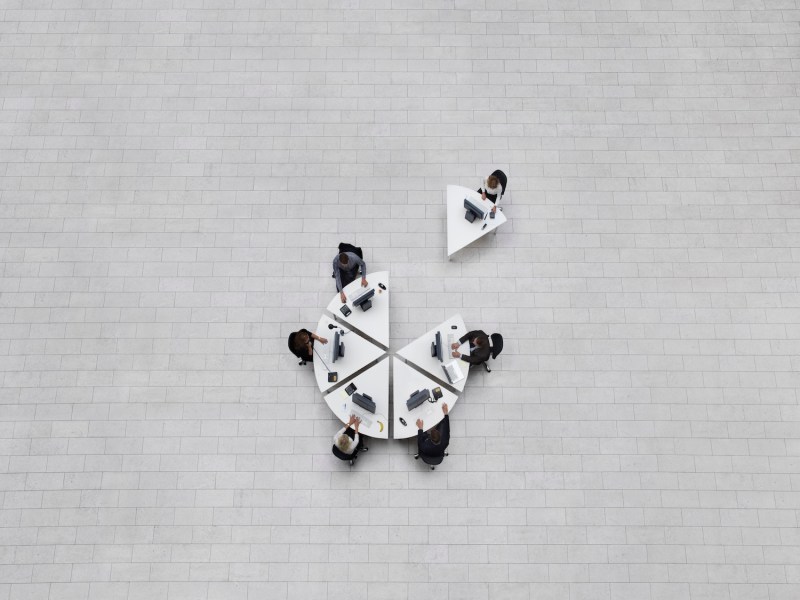 Geschäft aus der Vogelperspektive, Büro von oben gesehen, mit Mitarbeitern, die an ihren Arbeitsplätzen in einer Formation sitzen, die wie ein Kreis geformt ist, einer von ihren Kollegen weggezogen.