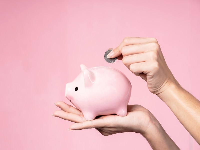 Nahaufnahme von Händen, die Münzen in ein Sparschwein werfen.