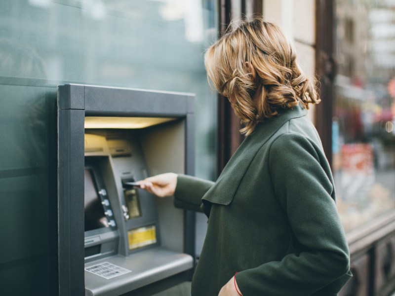 Eine June Frau hebt Geld am Bankautomaten ab.