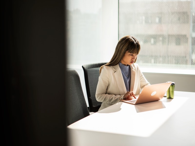 Eine Frau im Anzug sitzt im Büro und arbeitet am Laptop.
