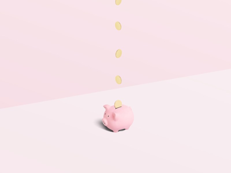 Rosa Sparschwein mit Goldmünzen, die von oben auf einem geteilten rosa Hintergrund hineinfallen.