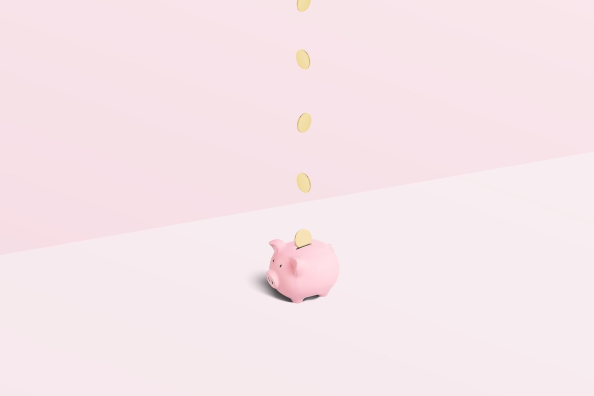 Rosa Sparschwein mit Goldmünzen, die von oben auf einem geteilten rosa Hintergrund hineinfallen.