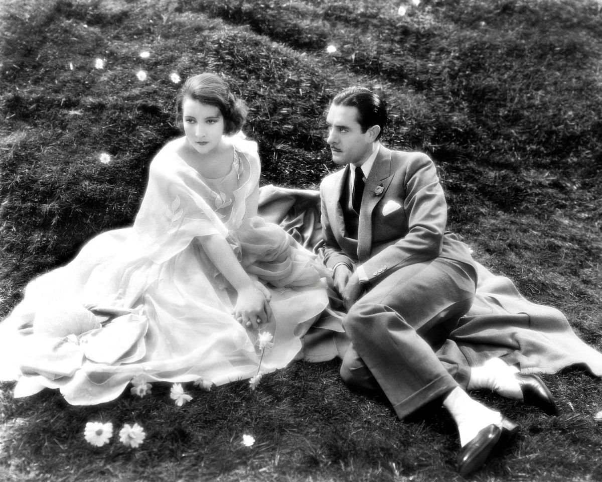 Frau und Mann sitzen im Kleid und Anzug auf der Wiese in Schwarz-Weiß-Foto.