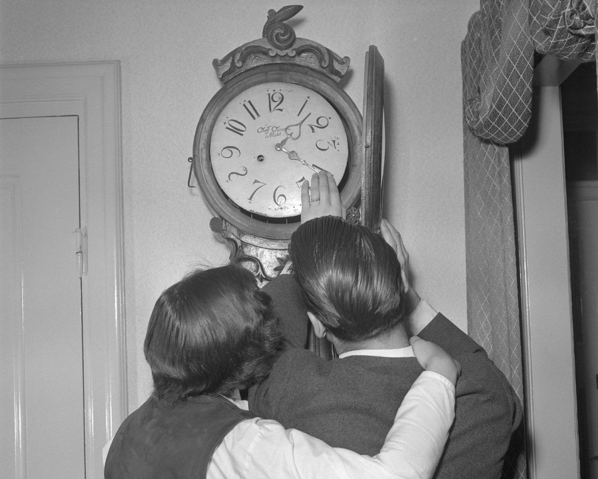 Frau und Mann schauen auf eine alte Wanduhr