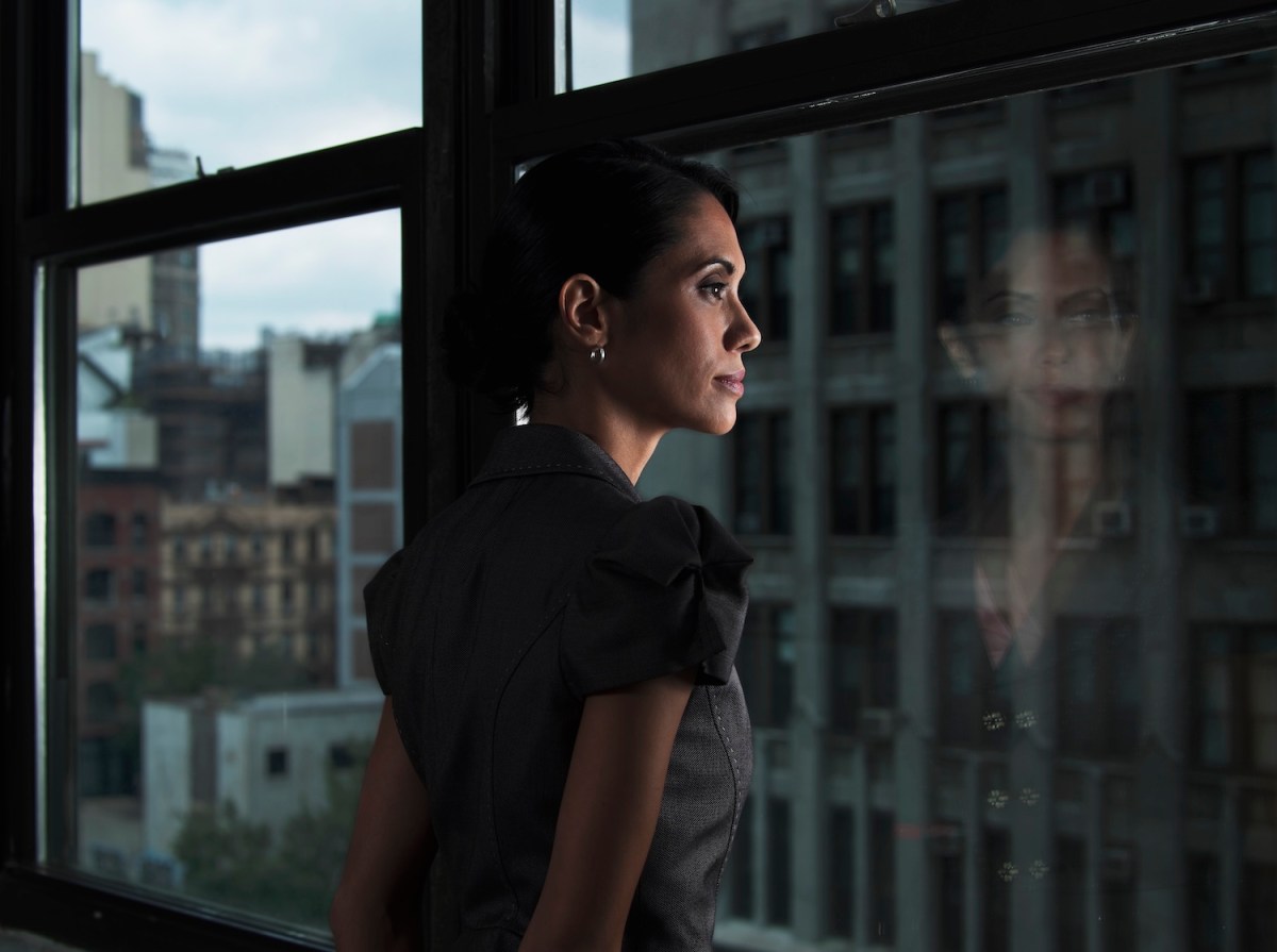 Eine Frau mit braunen Haaren schaut aus dem Büro aus dem Fenster.