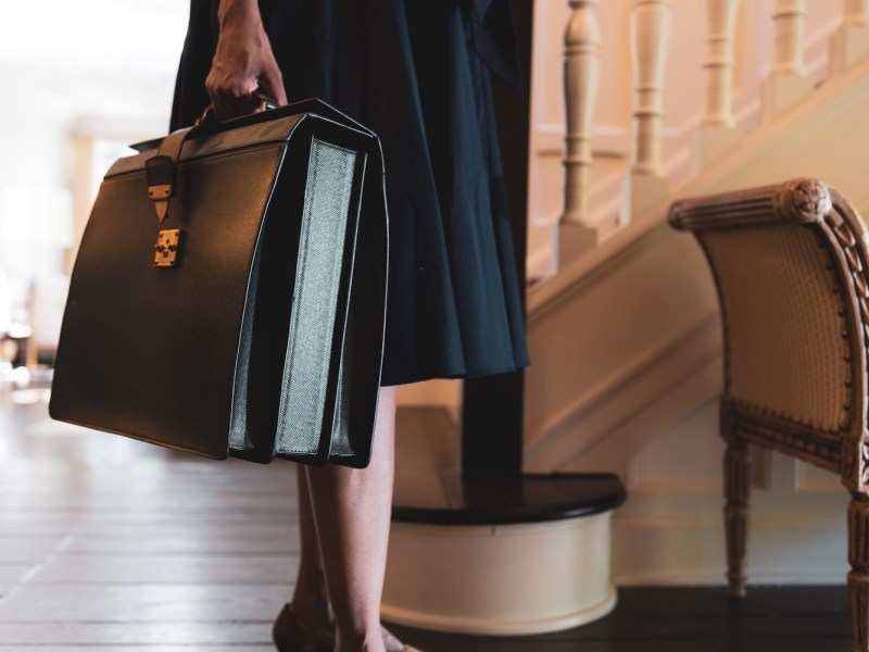 Gut gekleidete, berufstätige Frau trägt eine Aktentasche in der Hand.